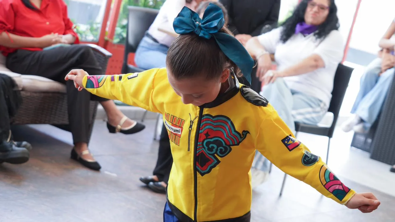 A girl dances with outstretched arms before the audience at a gathering.
