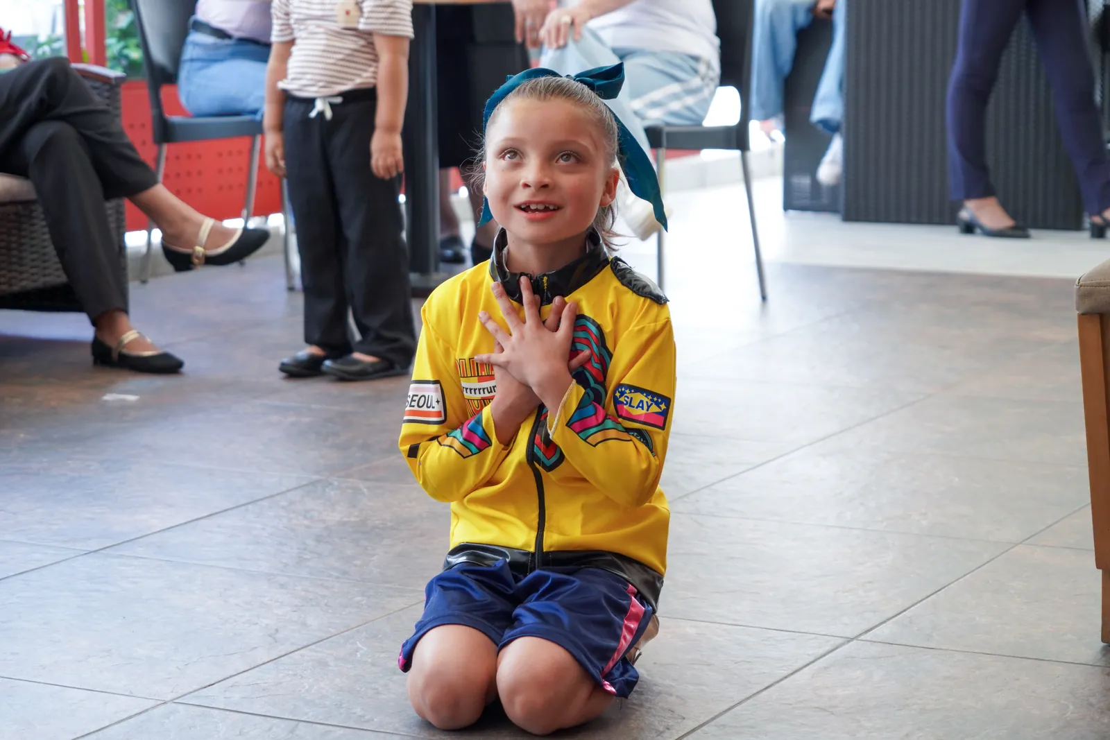 A girl celebrates, kneeling and smiling, during a gathering.