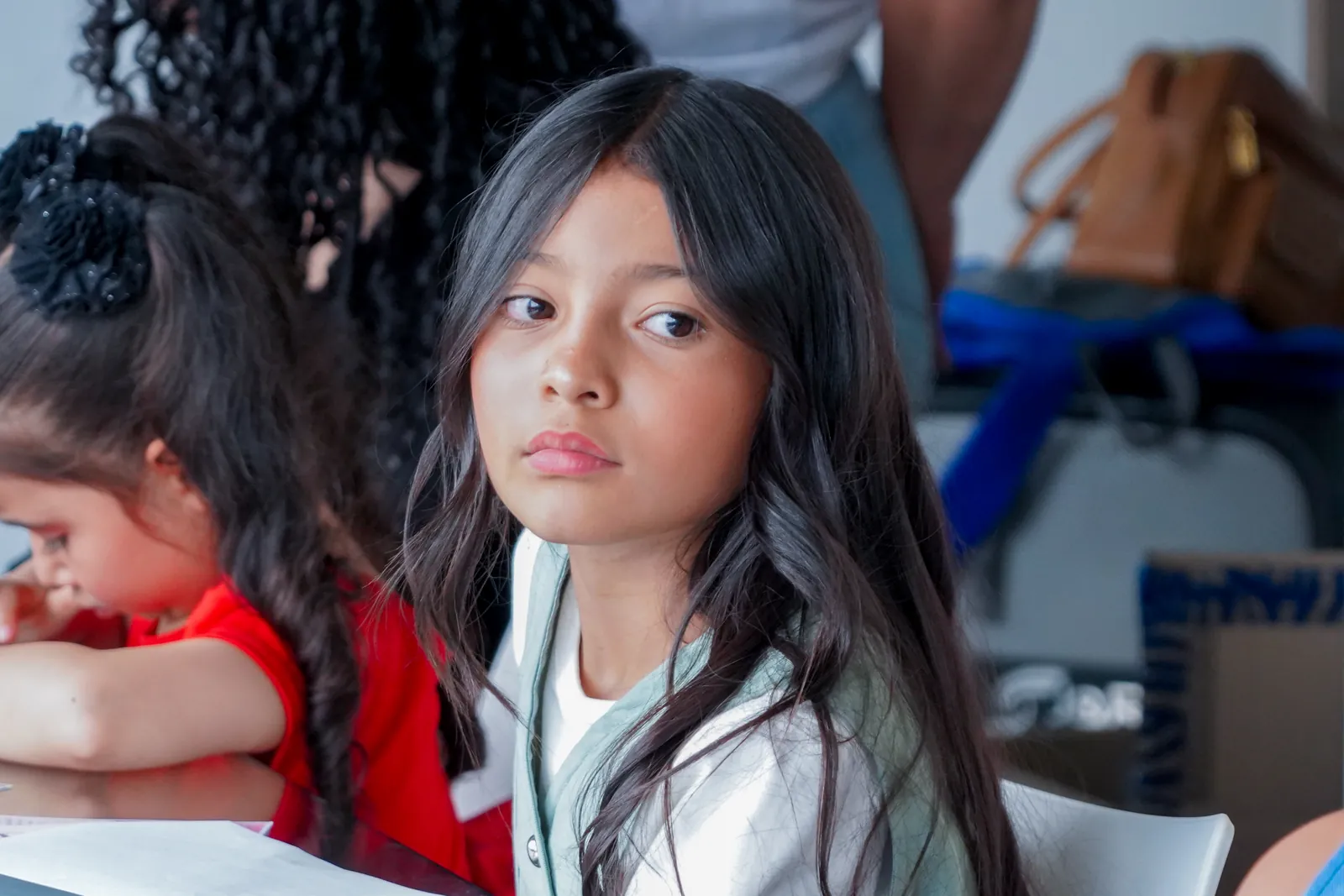 A girl looks at the camera while her peers work at the table.