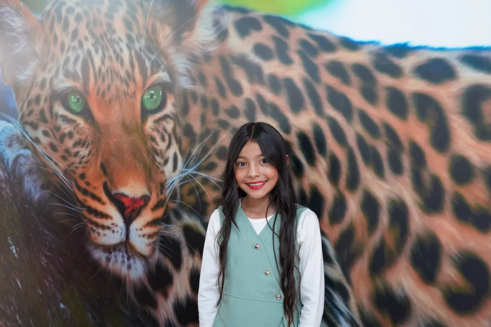 A smiling girl poses next to a leopard mural.